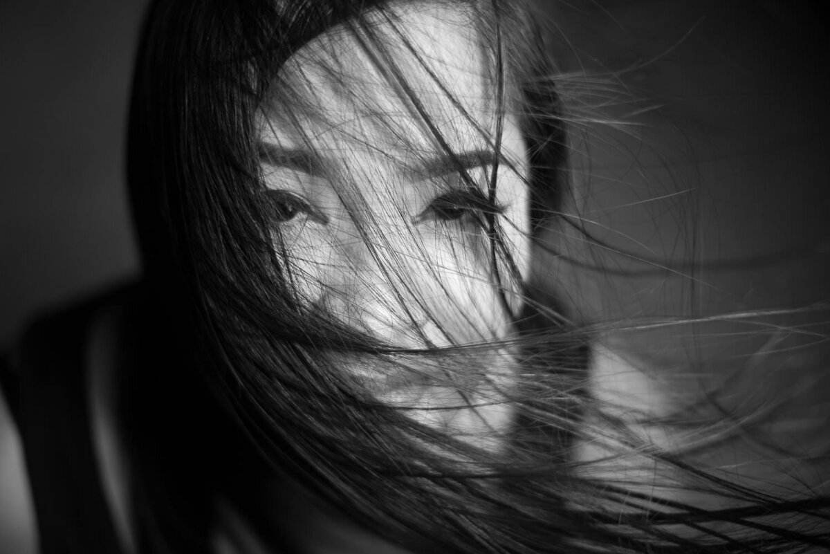Close-up editorial portrait of a woman with hair blowing across her face, creating a moody and mysterious atmosphere.