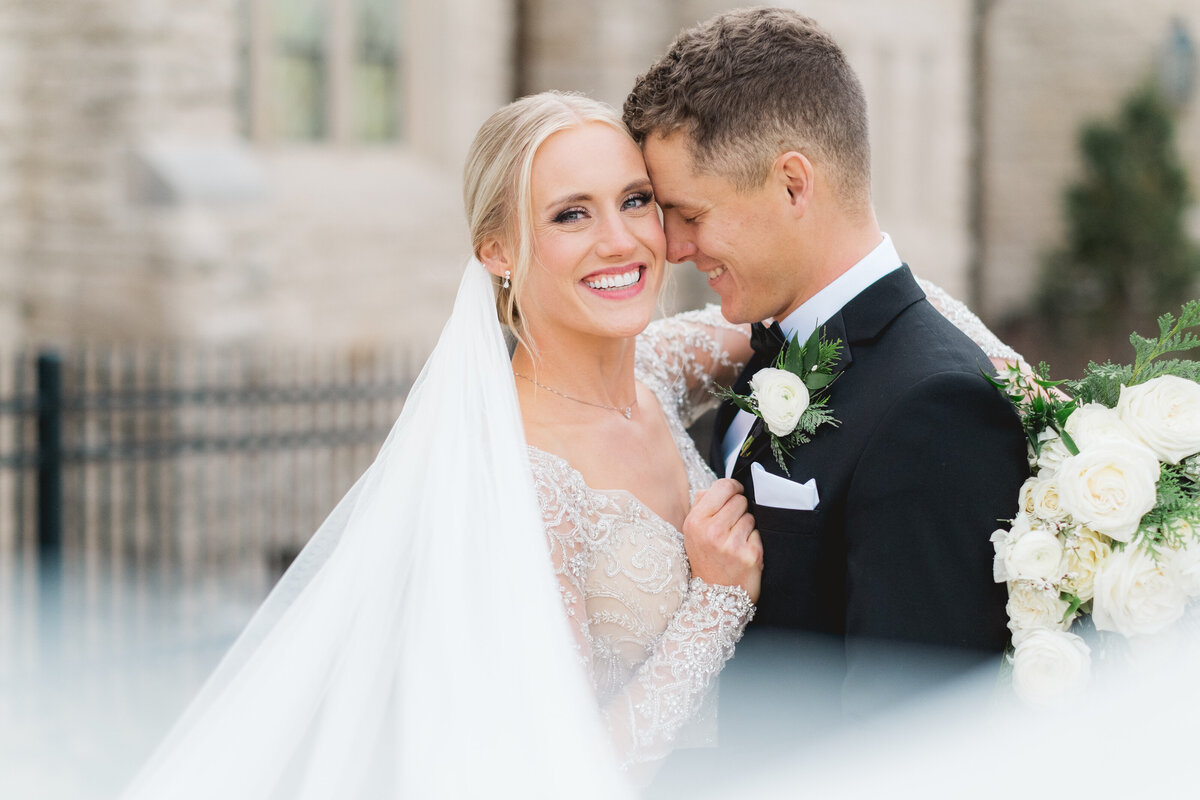 wedding couple wearing black tuxedo and white beaded gown hugging at St. Agnes Catholic Church