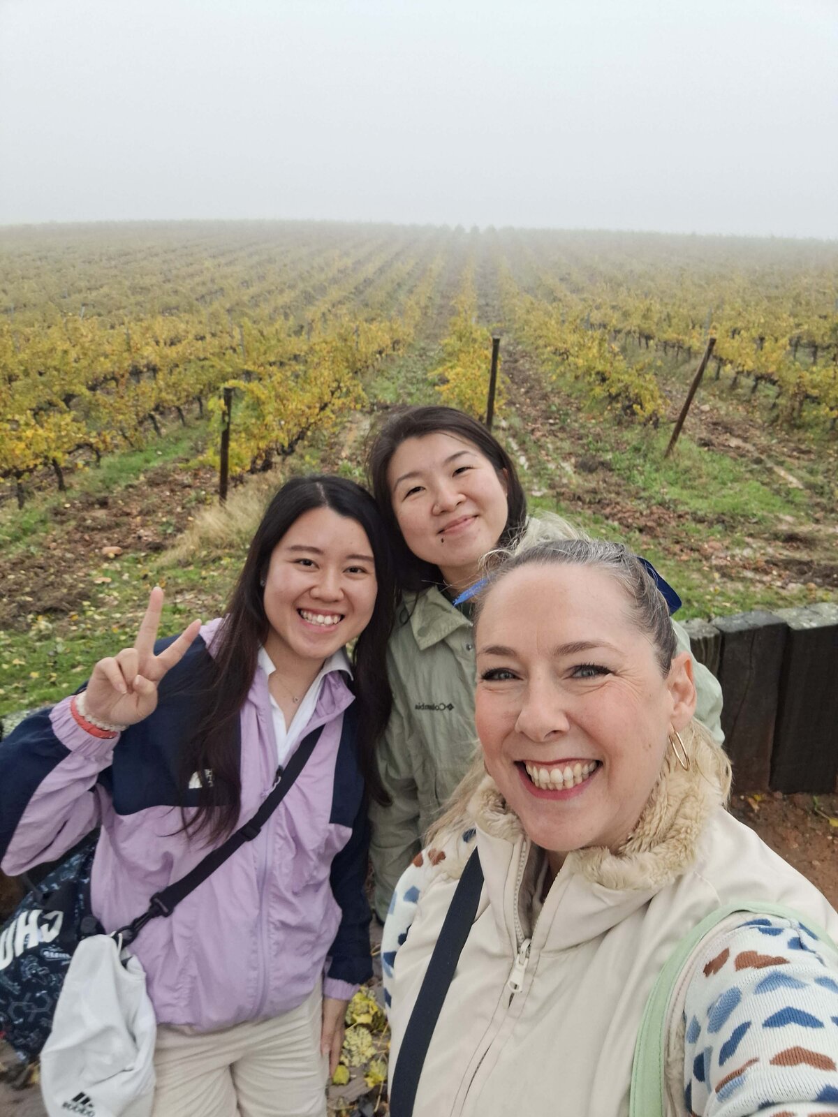 Maria Cristina and two women taking a photo together in with the beautiful winery landscape in the background.