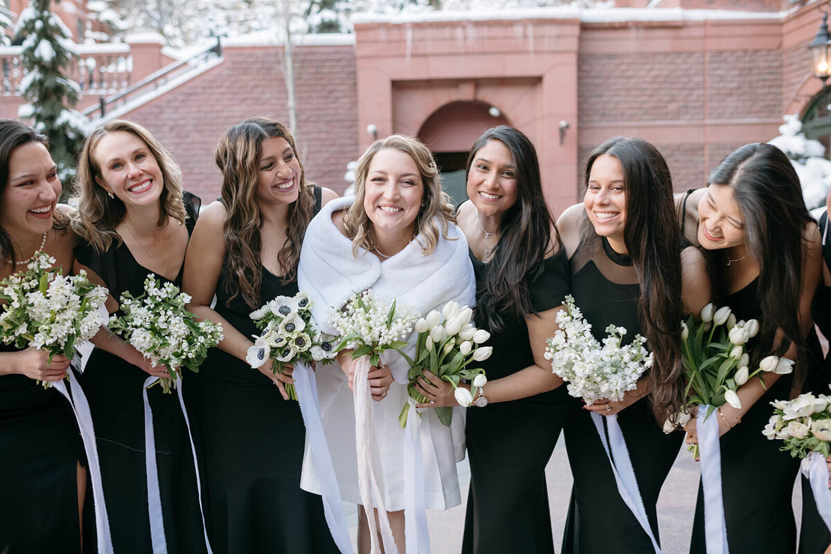 Bride and bridesmaids in black dresses pose together in celebration of the St. Regis Aspen wedding.
