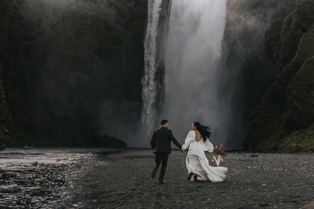 Holding hands, a walks toward a serene waterfall