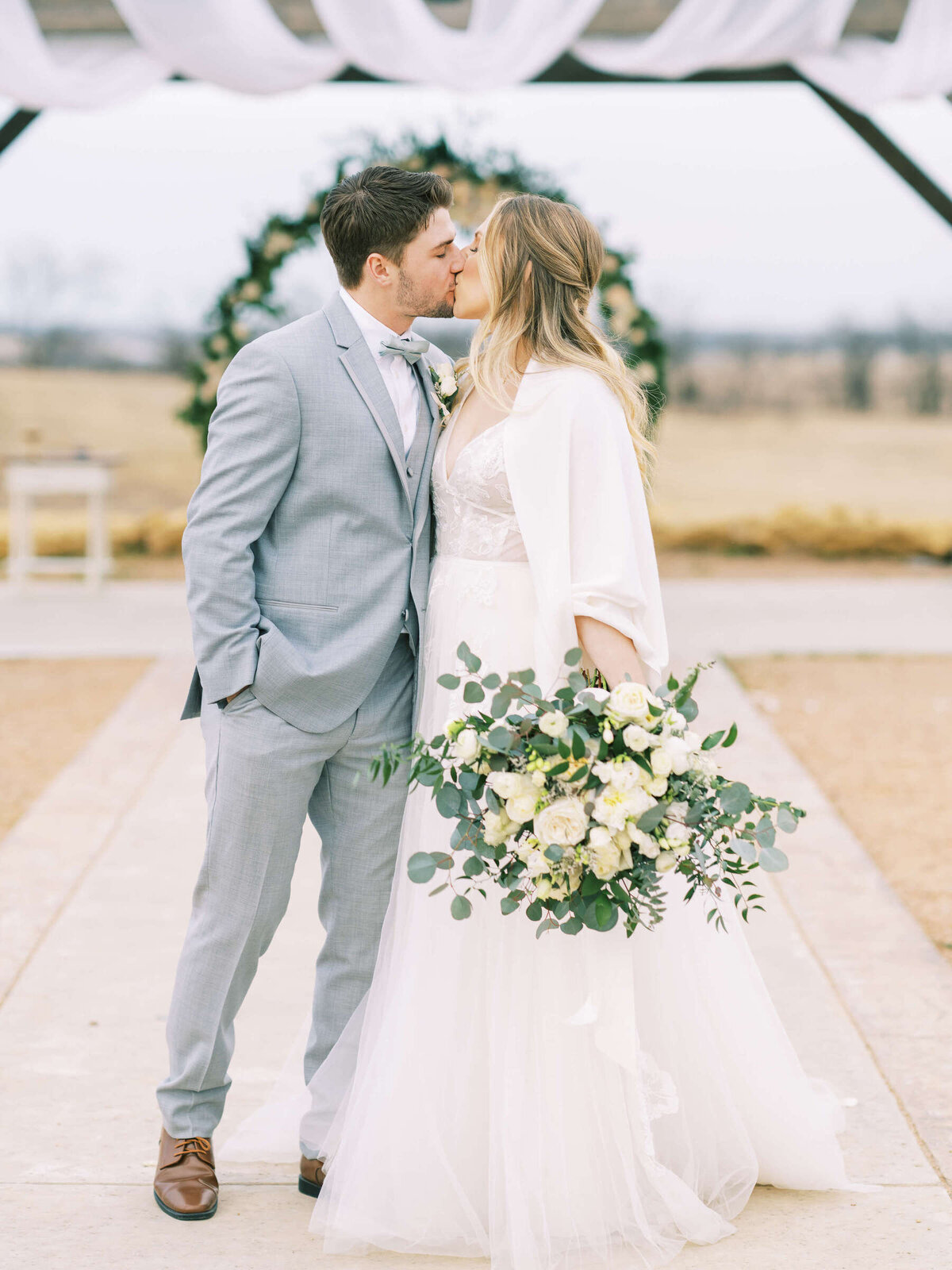 Bride and groom kiss at outdoor wedding in January