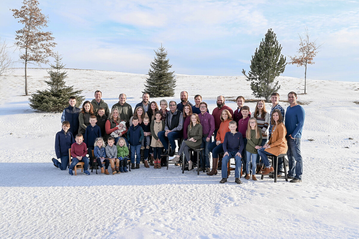 A big family sits and stands on a snowy hill with trees