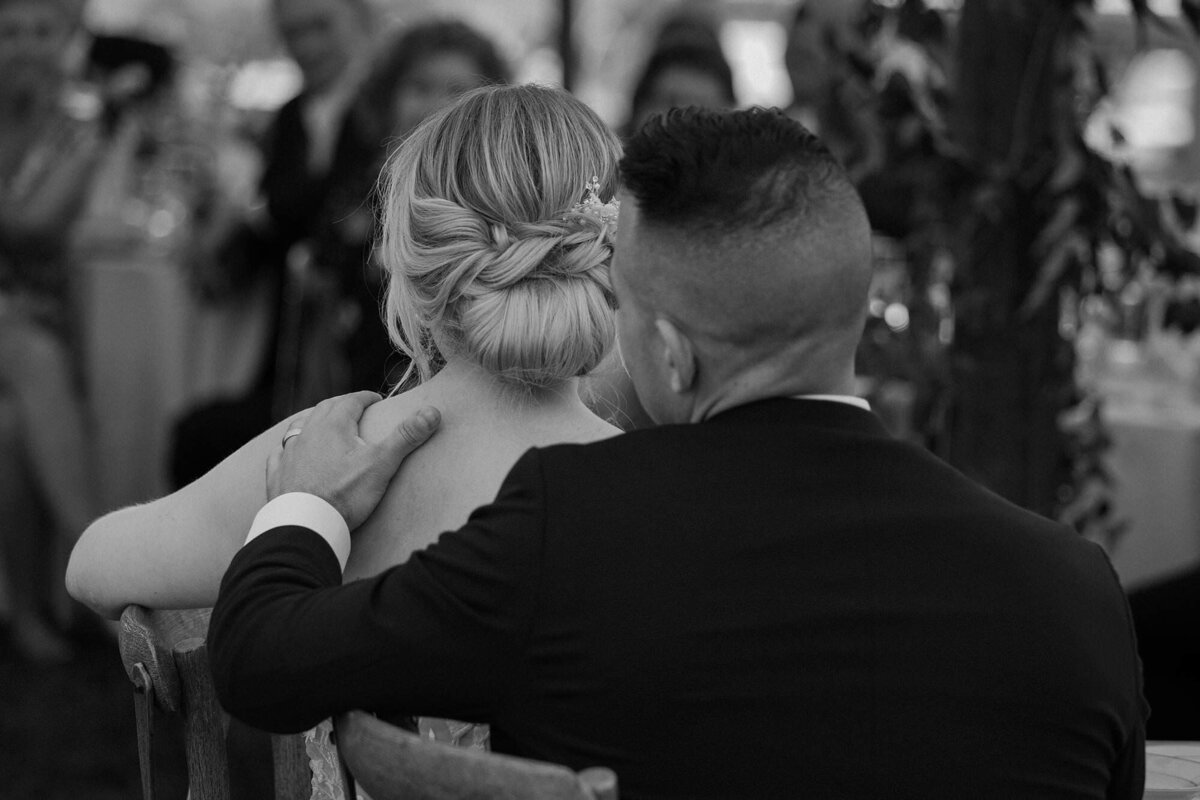 A wedding couple sitting down while one has their arm around the other 