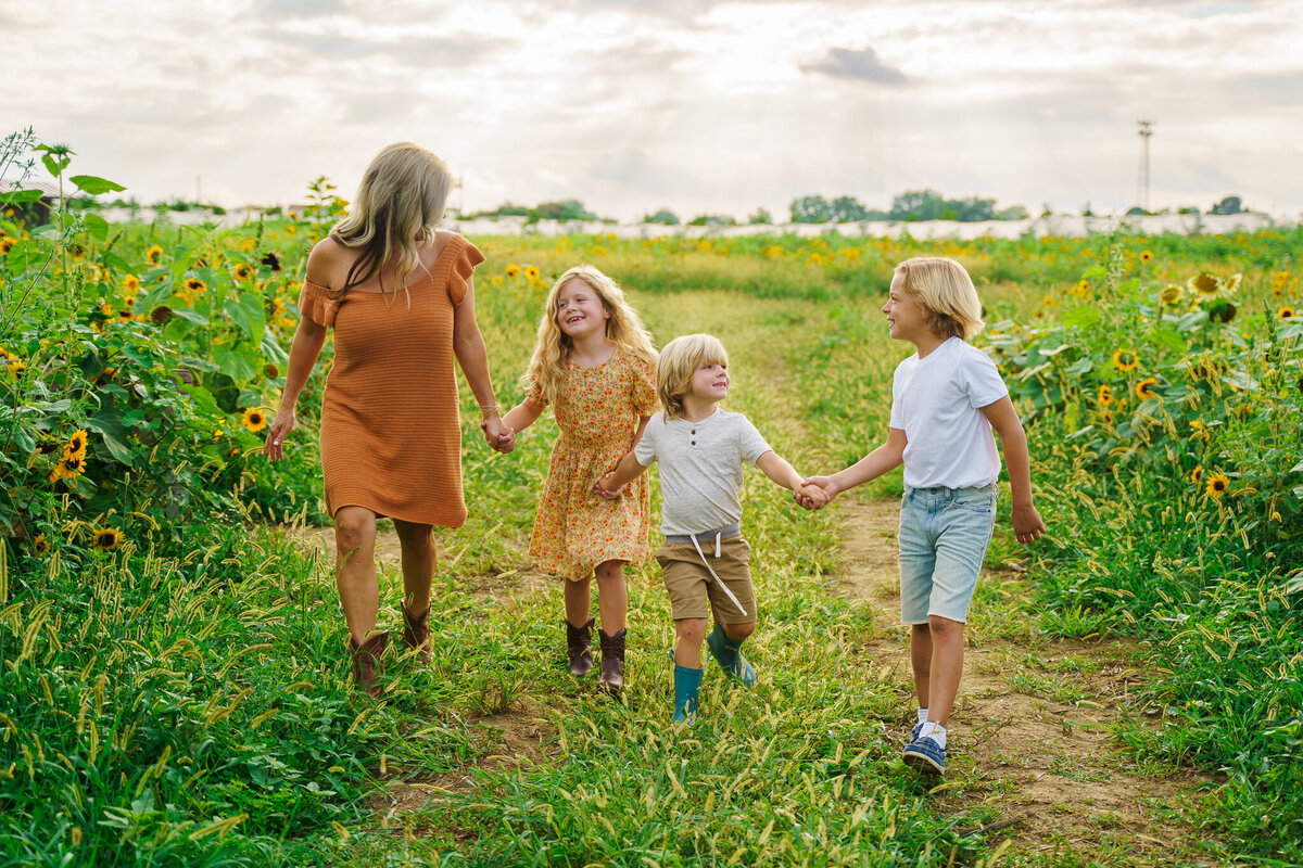 Family of four hold hands and walk together in a patch of sunflowers at Lynd Fruit Farms in Pataskala, Ohio.