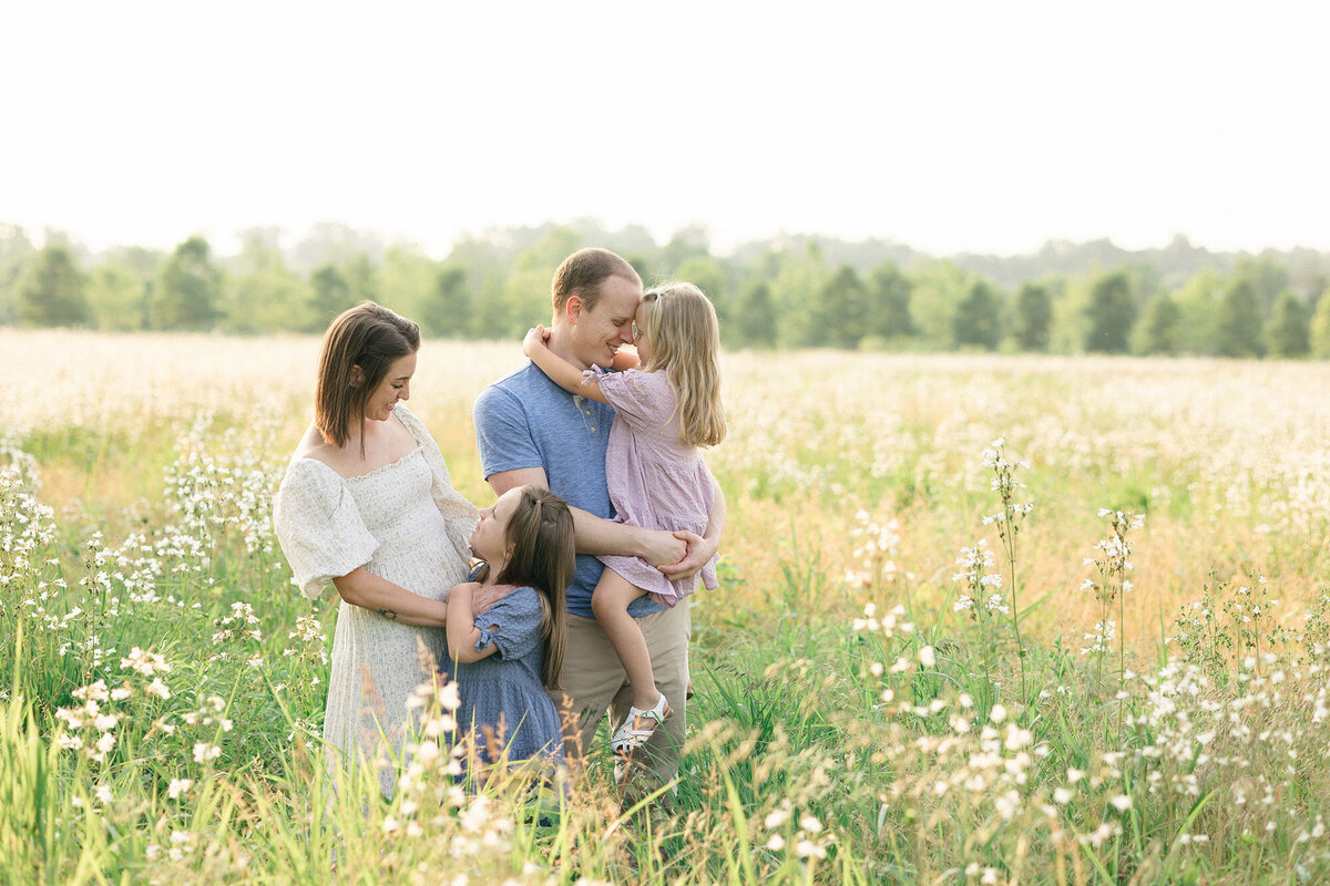 Family of four wearing coordinating spring colors standing in a field of white wild flowers