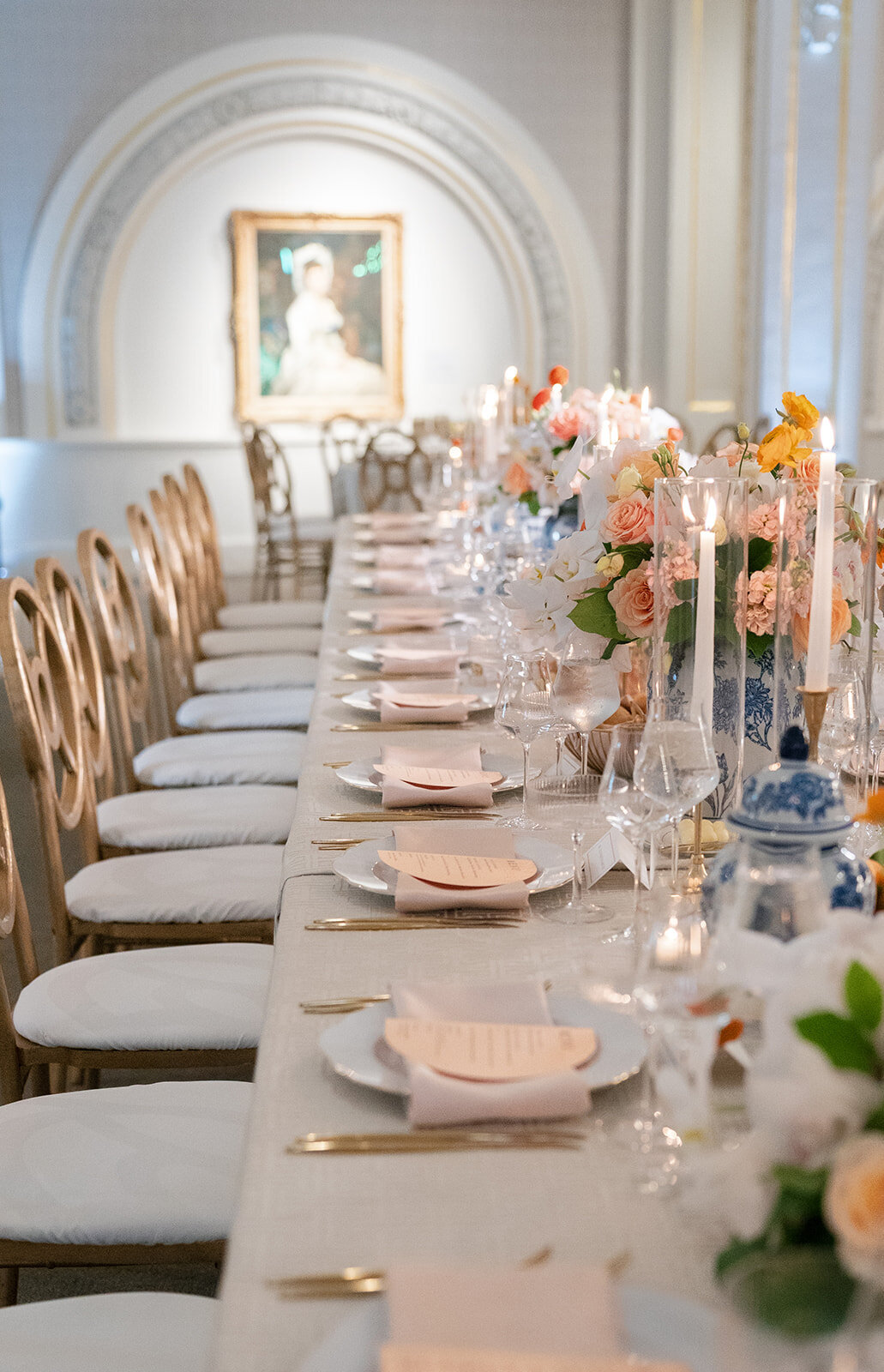 Long head table set up with bright citrus accents, chinoiserie cases, and elegant gold accents. 
