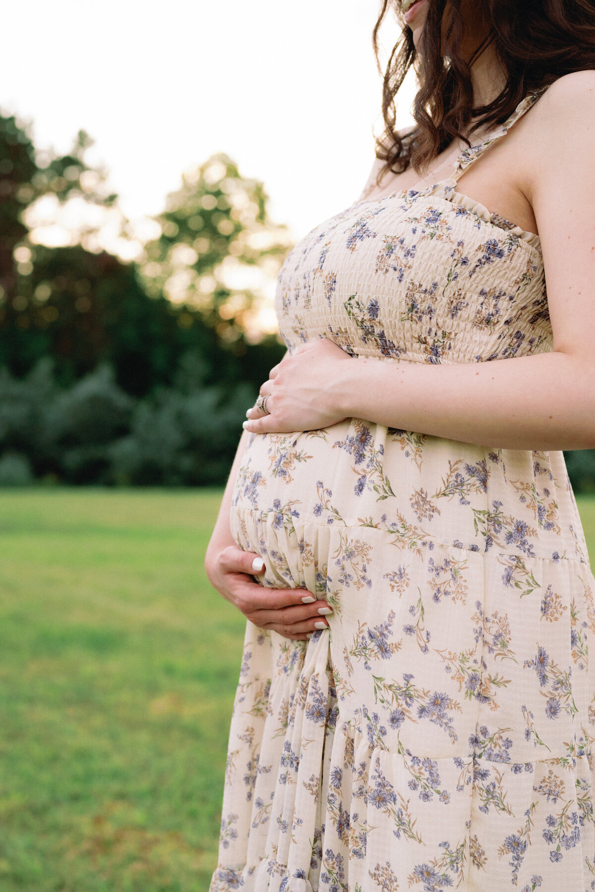 Close up of expecting mother holding baby bump in floral dress