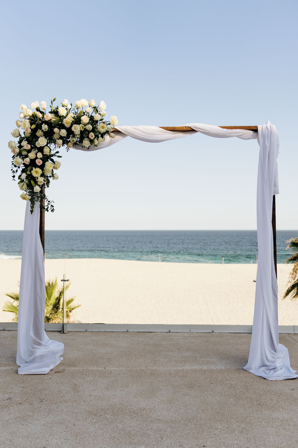 Floral arch with white drapery on a beach overlooking the ocean