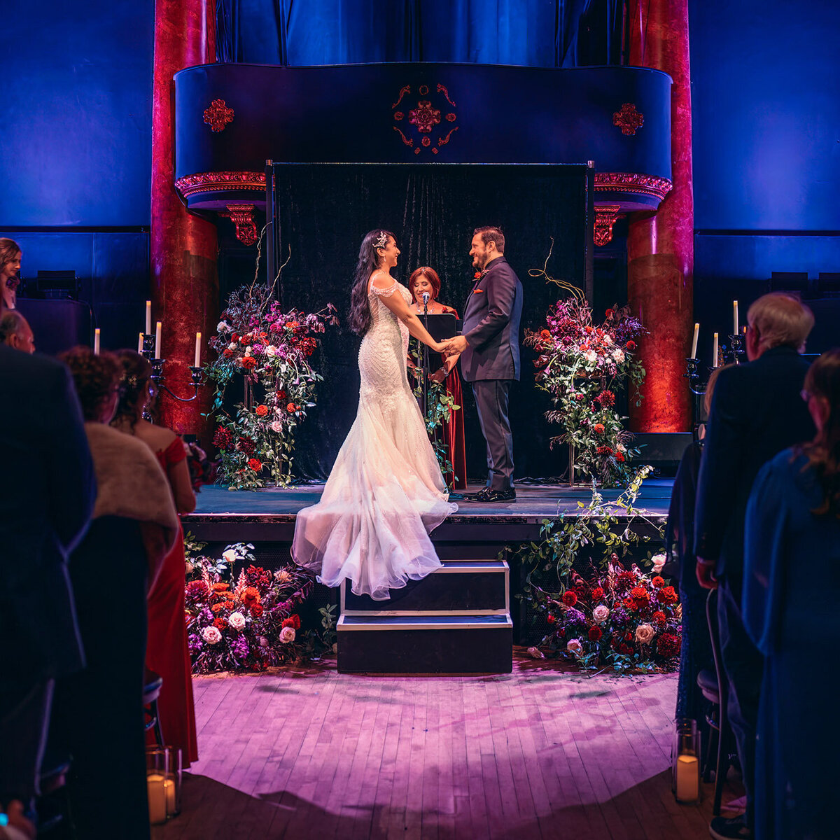 Indoor wedding ceremony with bold floral arrangements under purple lighting