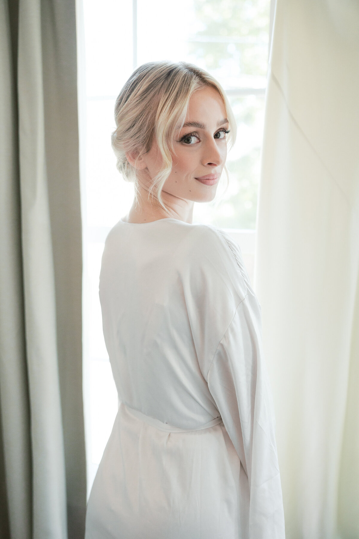 Bride looking back over her shoulder in soft bridal robe, beautifully lit in Dayton by a photographer from Philadelphia.