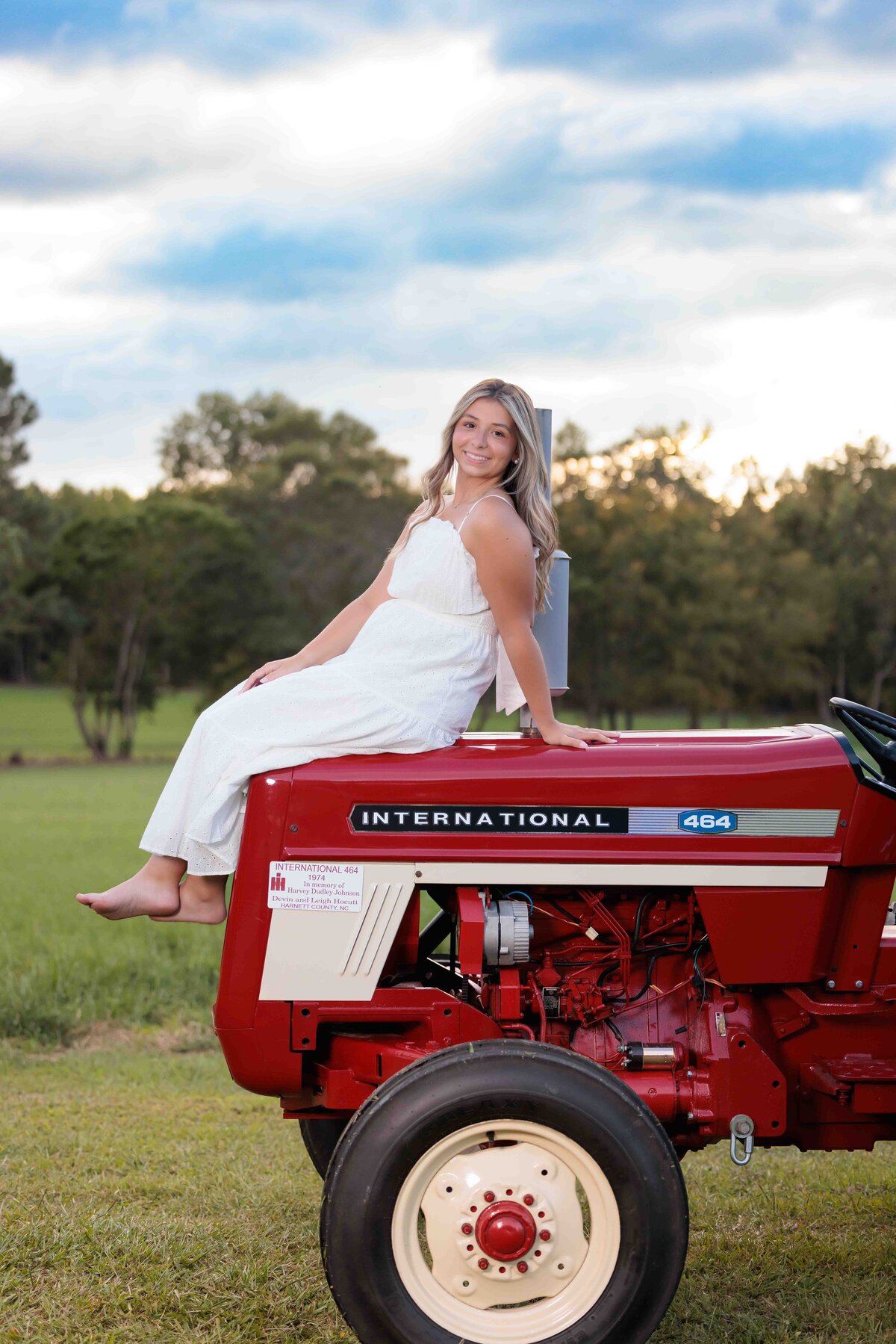 Country girl wearing white dress with red tractor for senior pictures..
