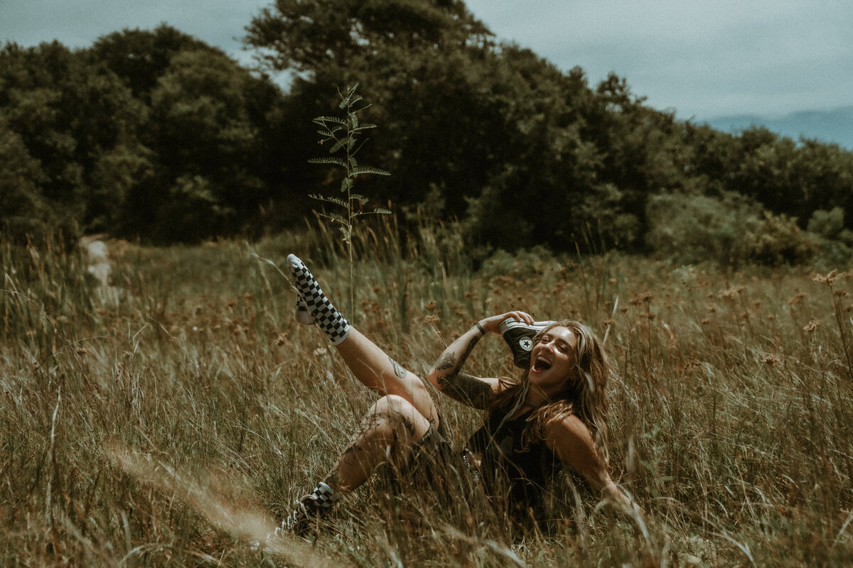 Grungy editorial portrait in Fort Pickens Florida — girl in field holding shoe to ear, cinematic moody film style