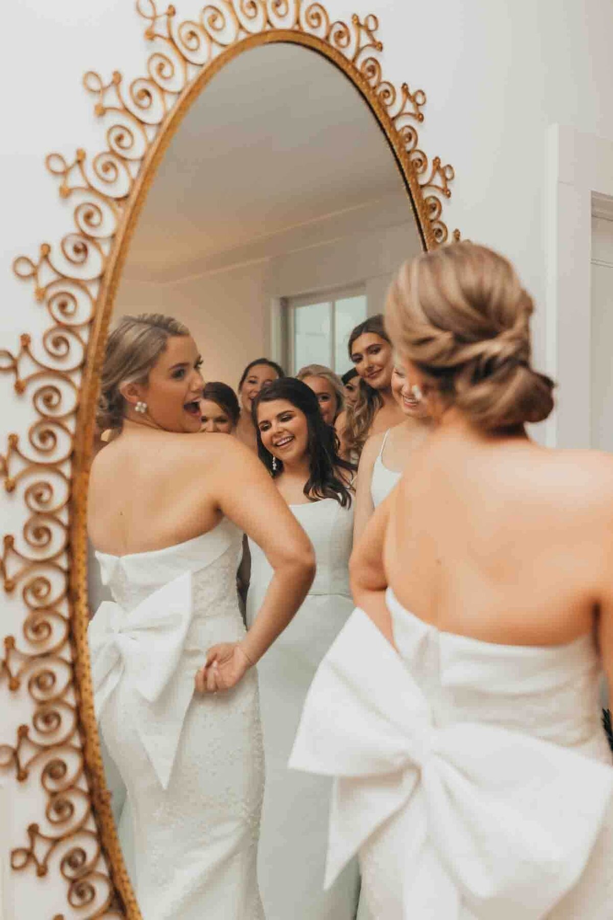 bride admires her dress in vintage mirror while bridesmaids dote on her.