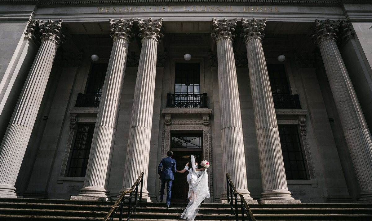 A bride and groom walking up the steps of their town hall.