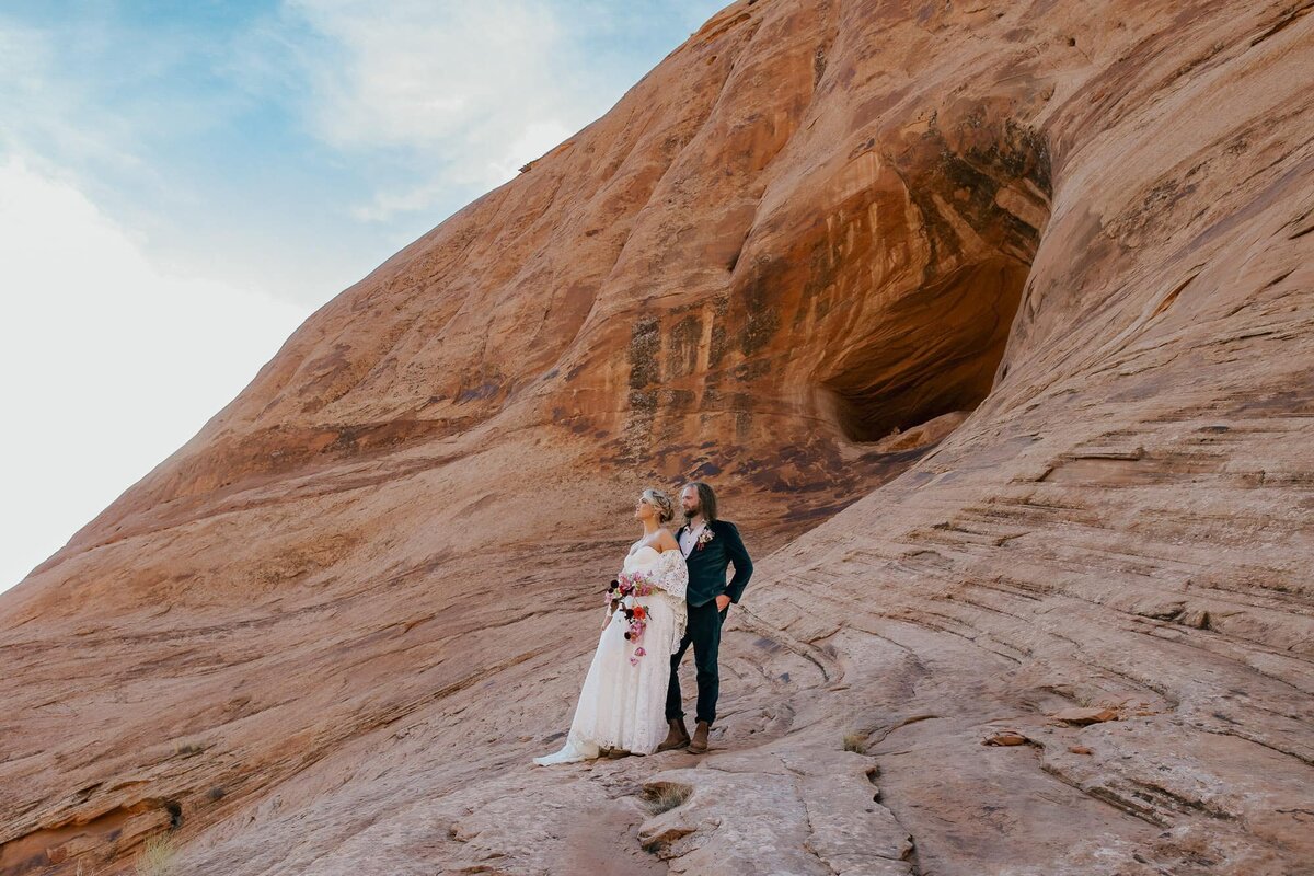 A bride and groom stand on red rocks in the Moab desert during their Adventure elopement in Utah