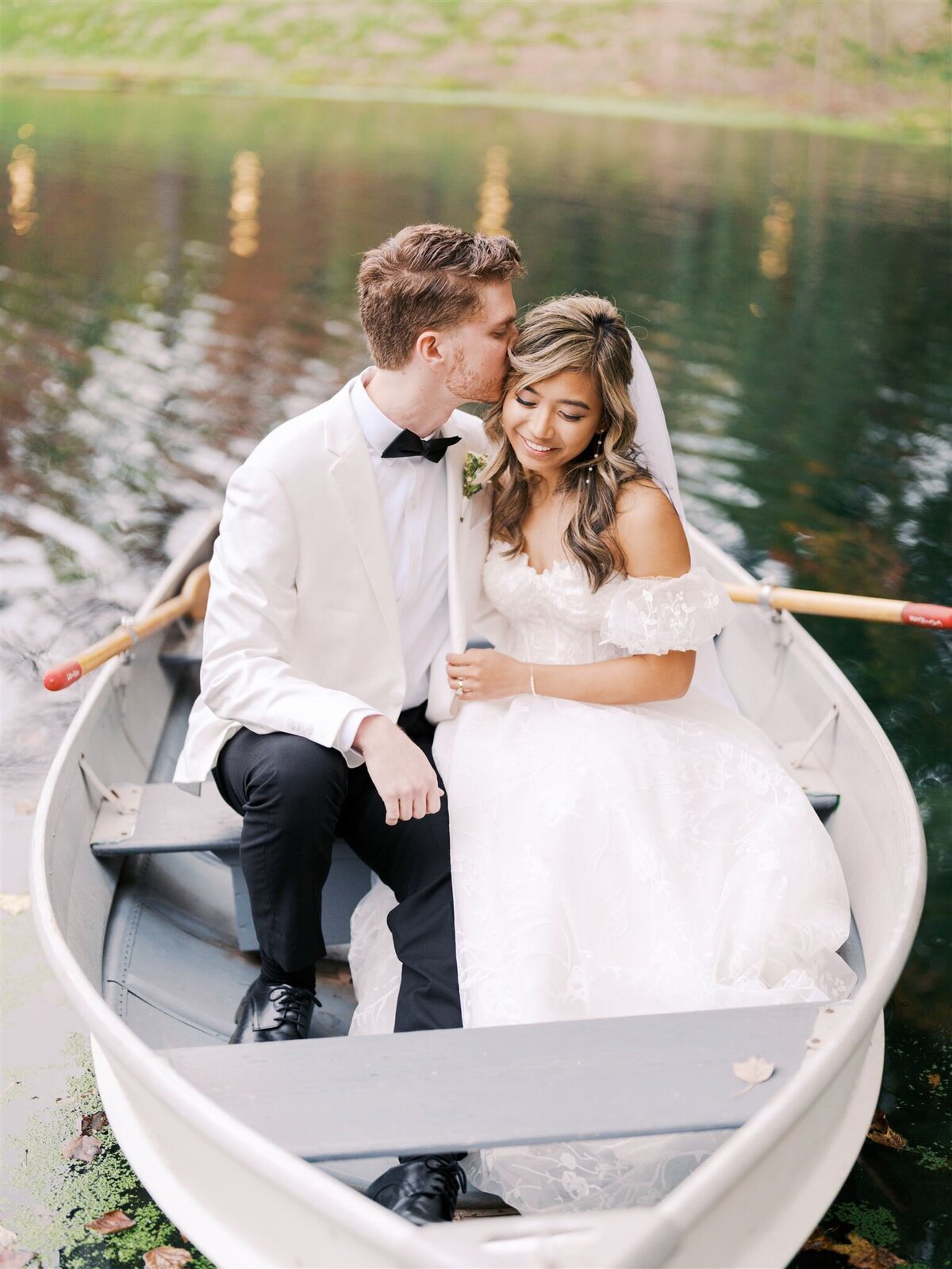 A romantic couple nestled together in a row boat on the water at Piney Grove Ranch, surrounded by autumn colors during a beautiful fall wedding, captured by North Carolina wedding photographer Jessica Leigh Mason.