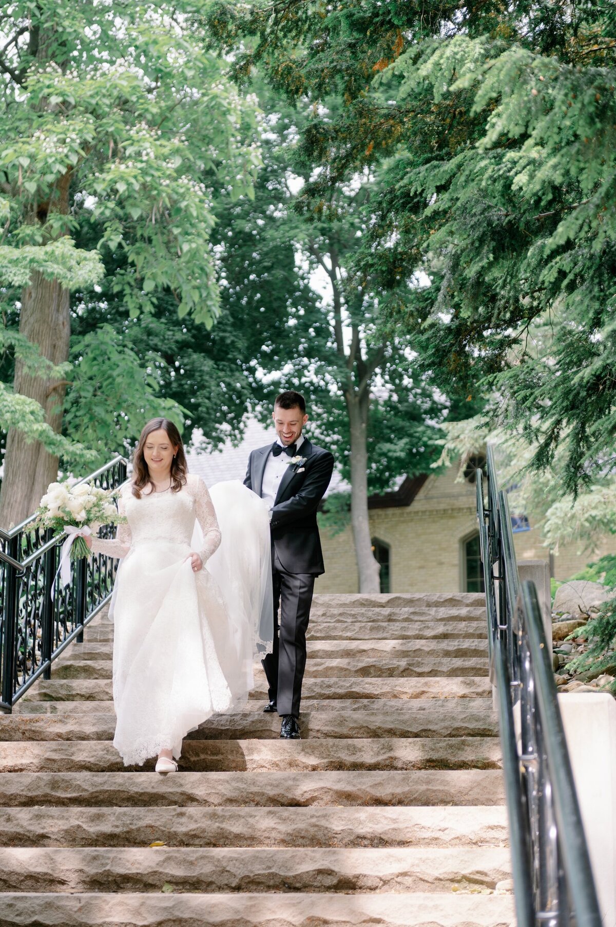 groom helping bride with dress train while she walks down steps