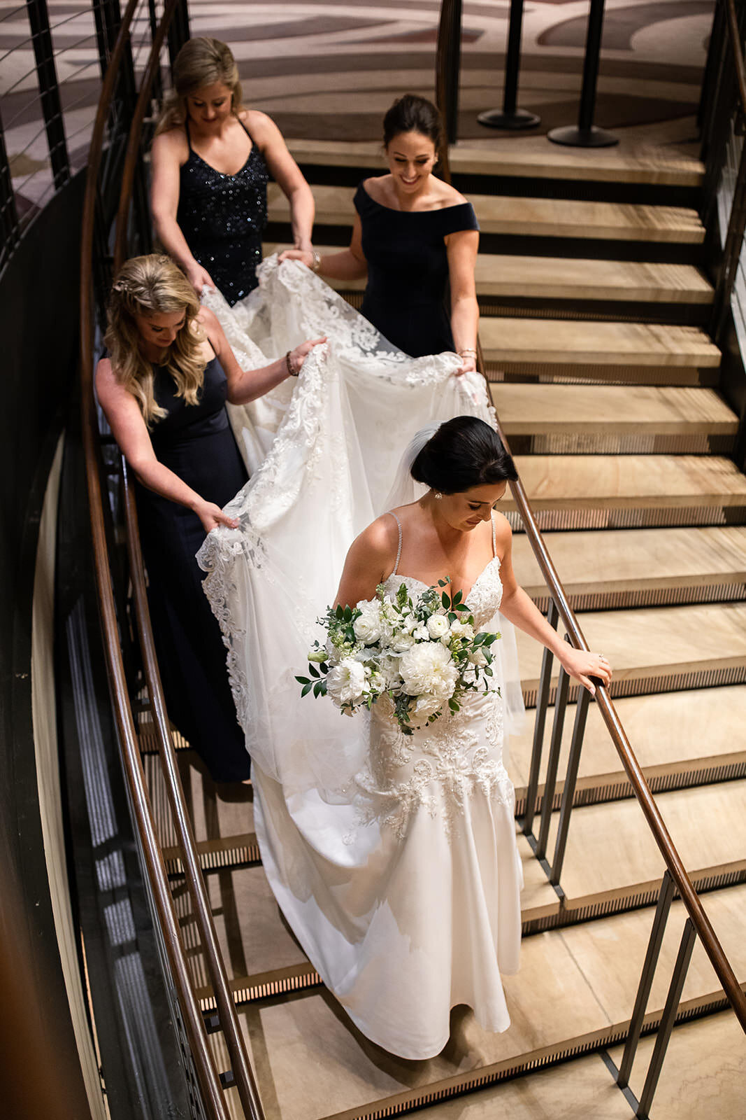 Bride walking down grand staircase with flowers in hand