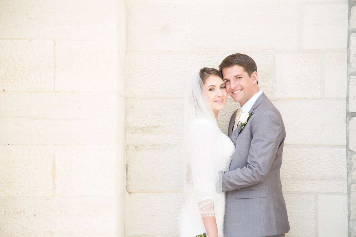 light and airy wedding photography of a bride  with a veil and groom  in a gray suit in front of a stone wall