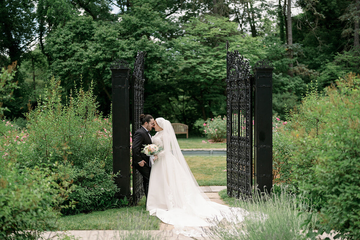 Bride and groom posing by the iconic wrought iron gate at Henry Ford Estate in Dearborn Michigan for timeless wedding photos.