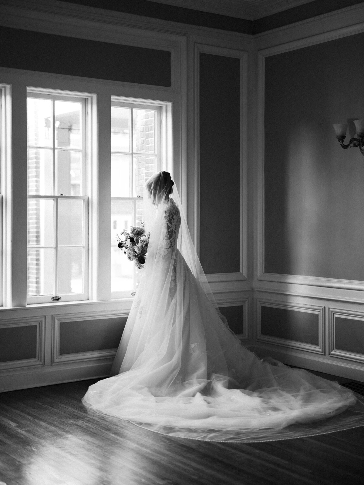 Editorial bride in long sleeve lace dress looking at flowers by window
