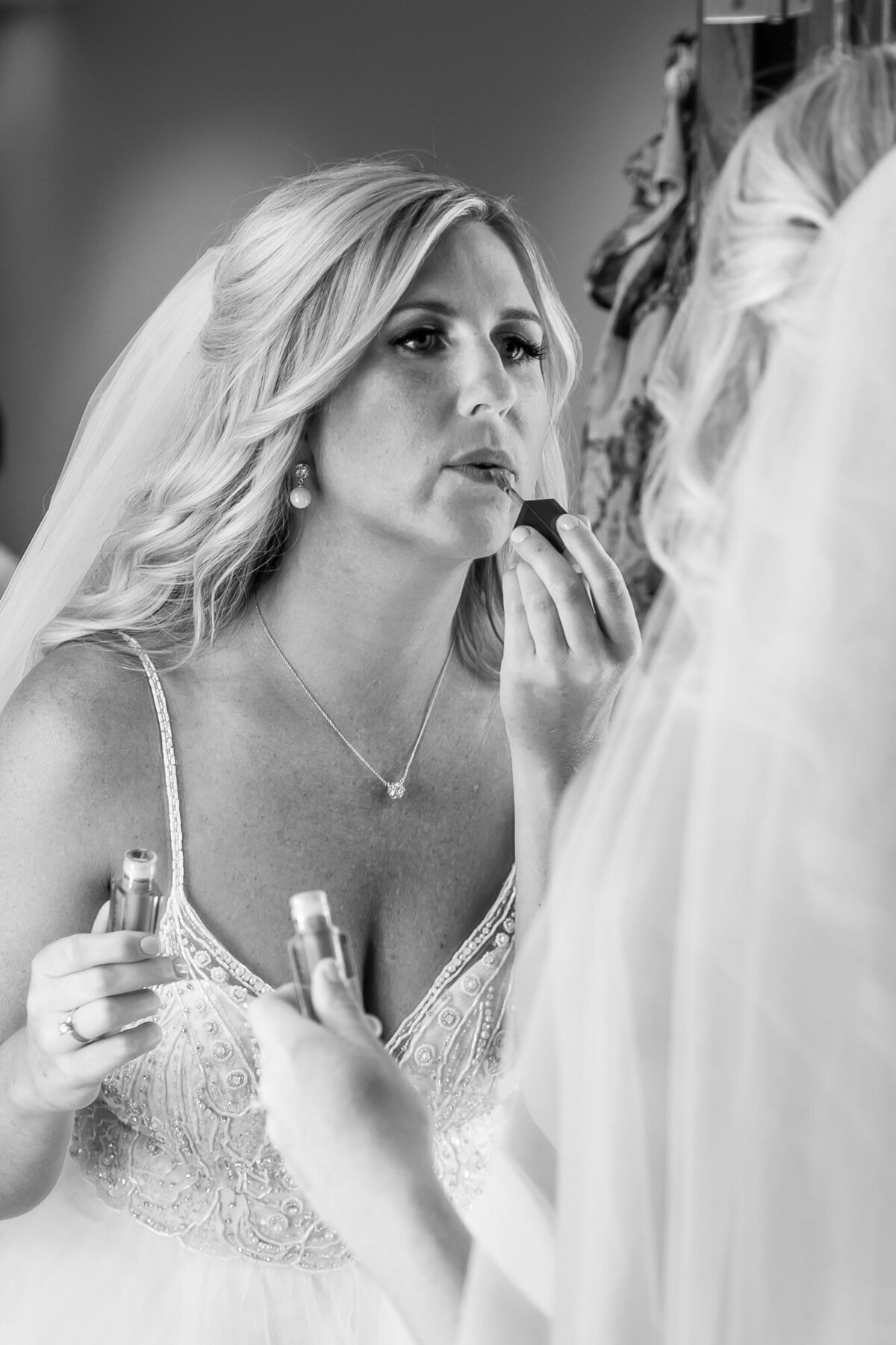 bride applies her lipstick in mirror in black and white image