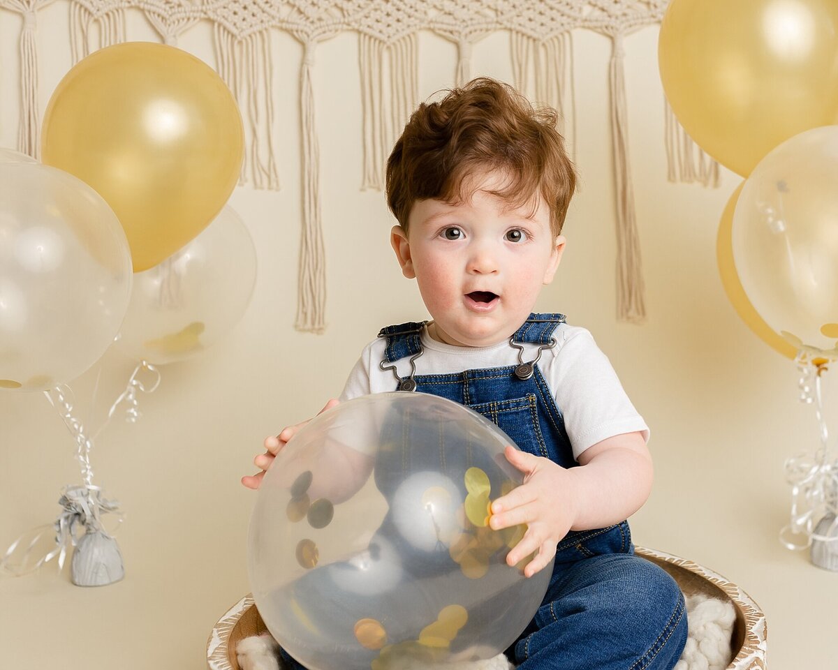 baby boy holding confetti balloon for milestone first birthday session near portland oregon
