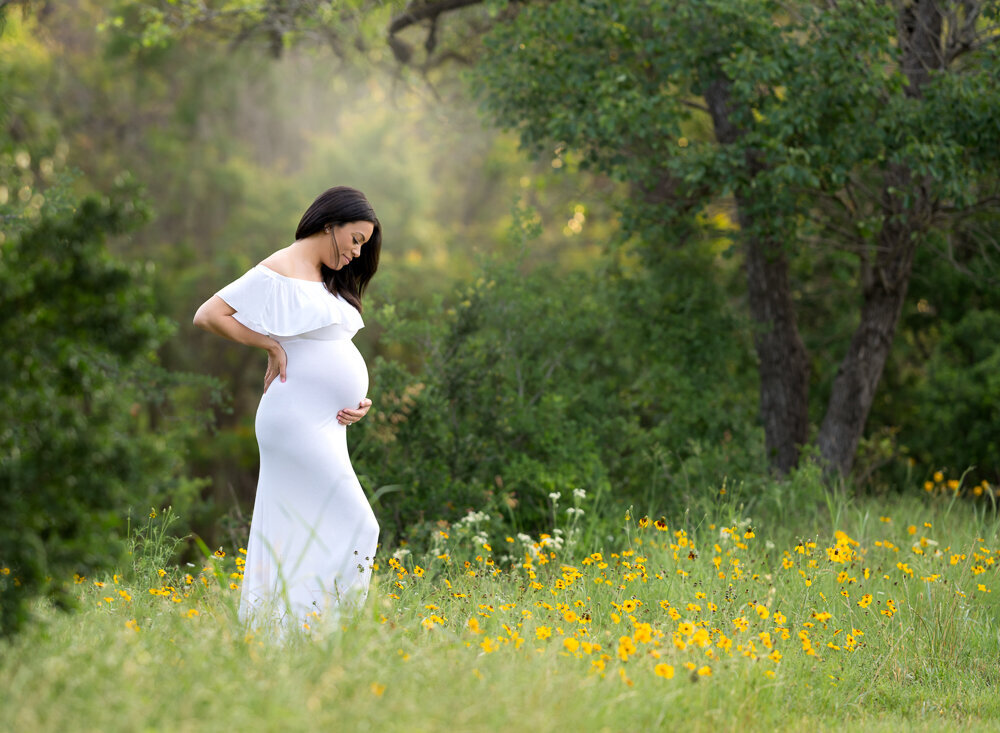 Expecting mother in a white dress surrounded by wildflowers in Cedar Park, Texas during spring maternity session