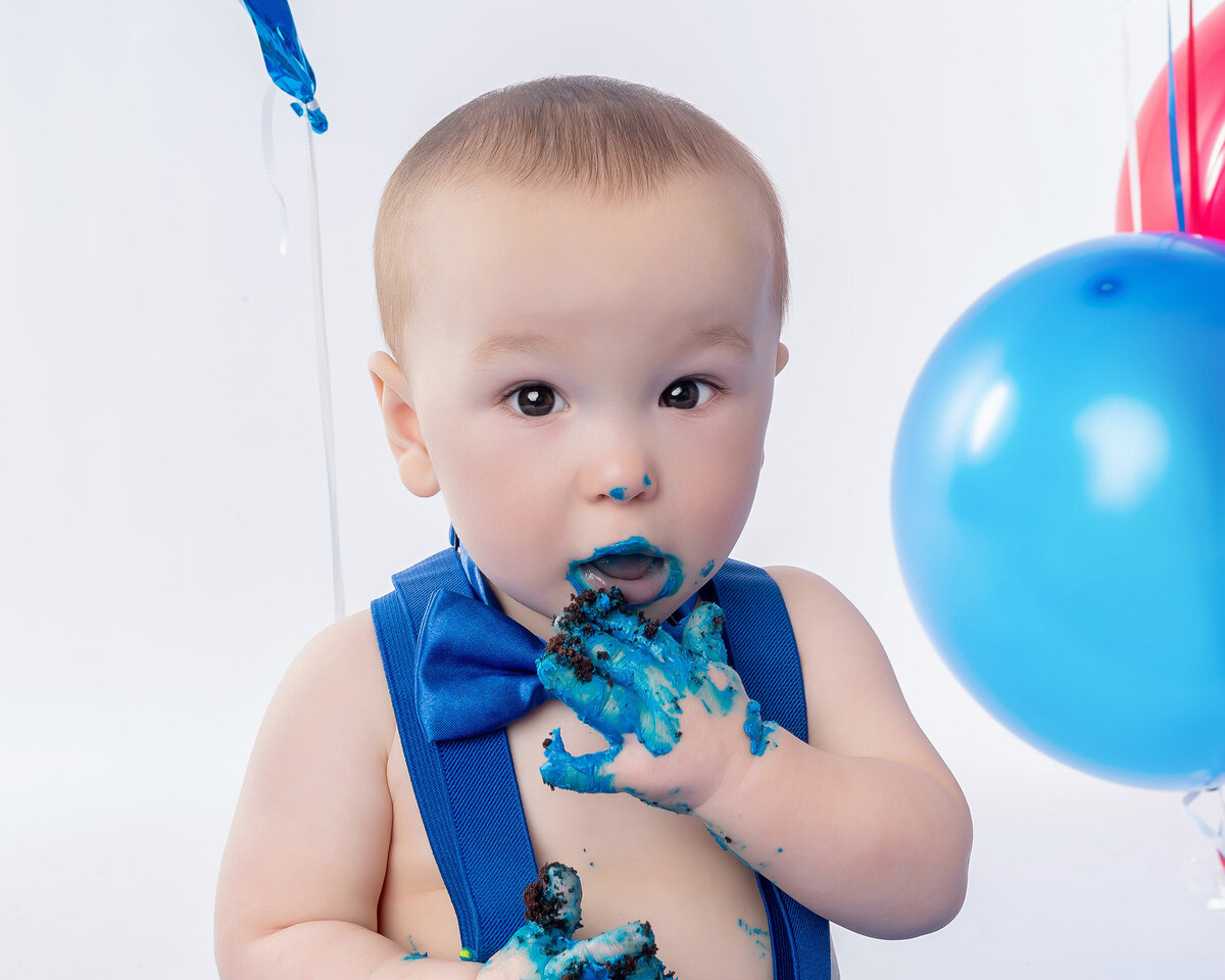 Baby boy eats frosting off his hands during a cake smash with an Iowa Milestone Photographer