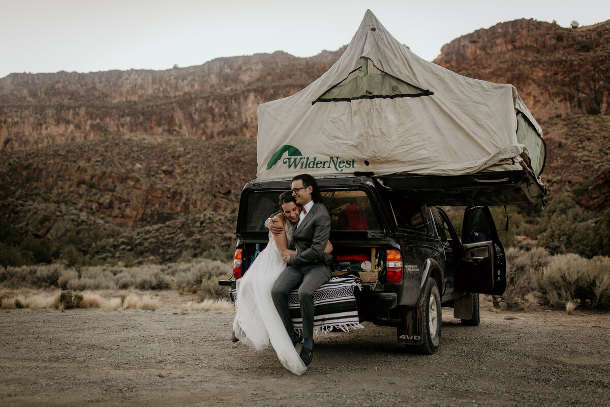 bride and groom sitting on a truck with a tent on top