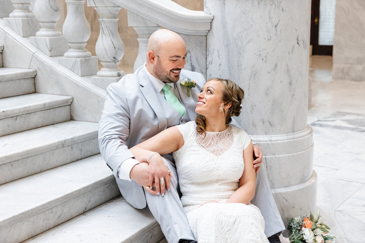 Bride and groom look lovingly into each others eyes as the snuggle together on the grand steps at the Utah State Capitol building.