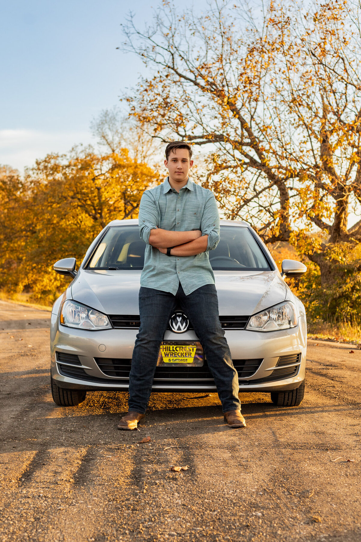 A senior guy sitting on the hood of his car crossing his arm in Lawrence, KS