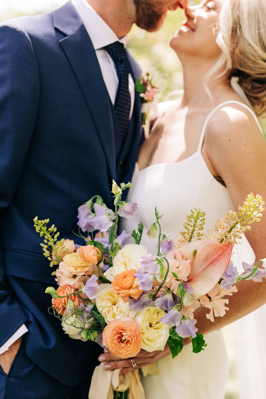 A close up of a bride's flower bouquet and the bride and groom embracing.