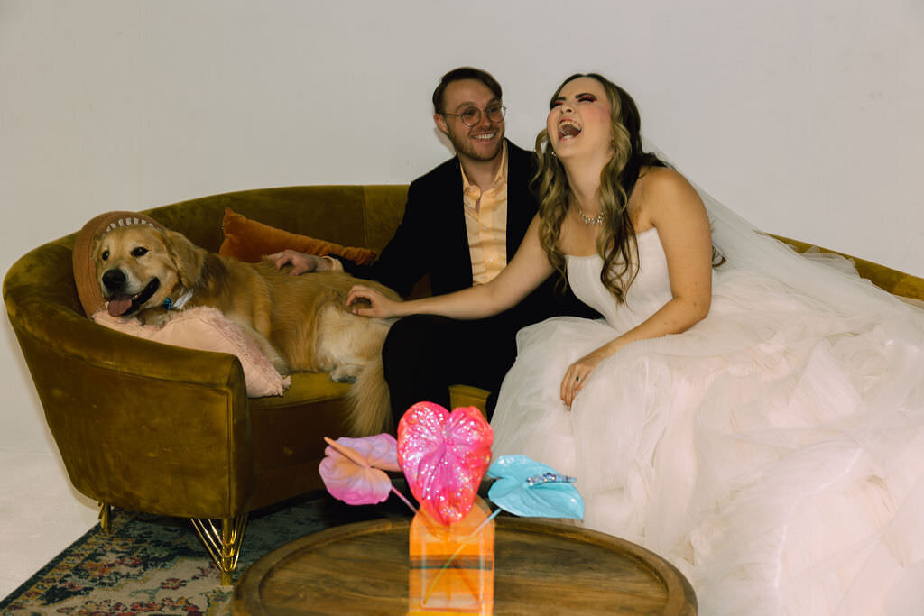 A newlywed couple sitting on a couch with a dog.