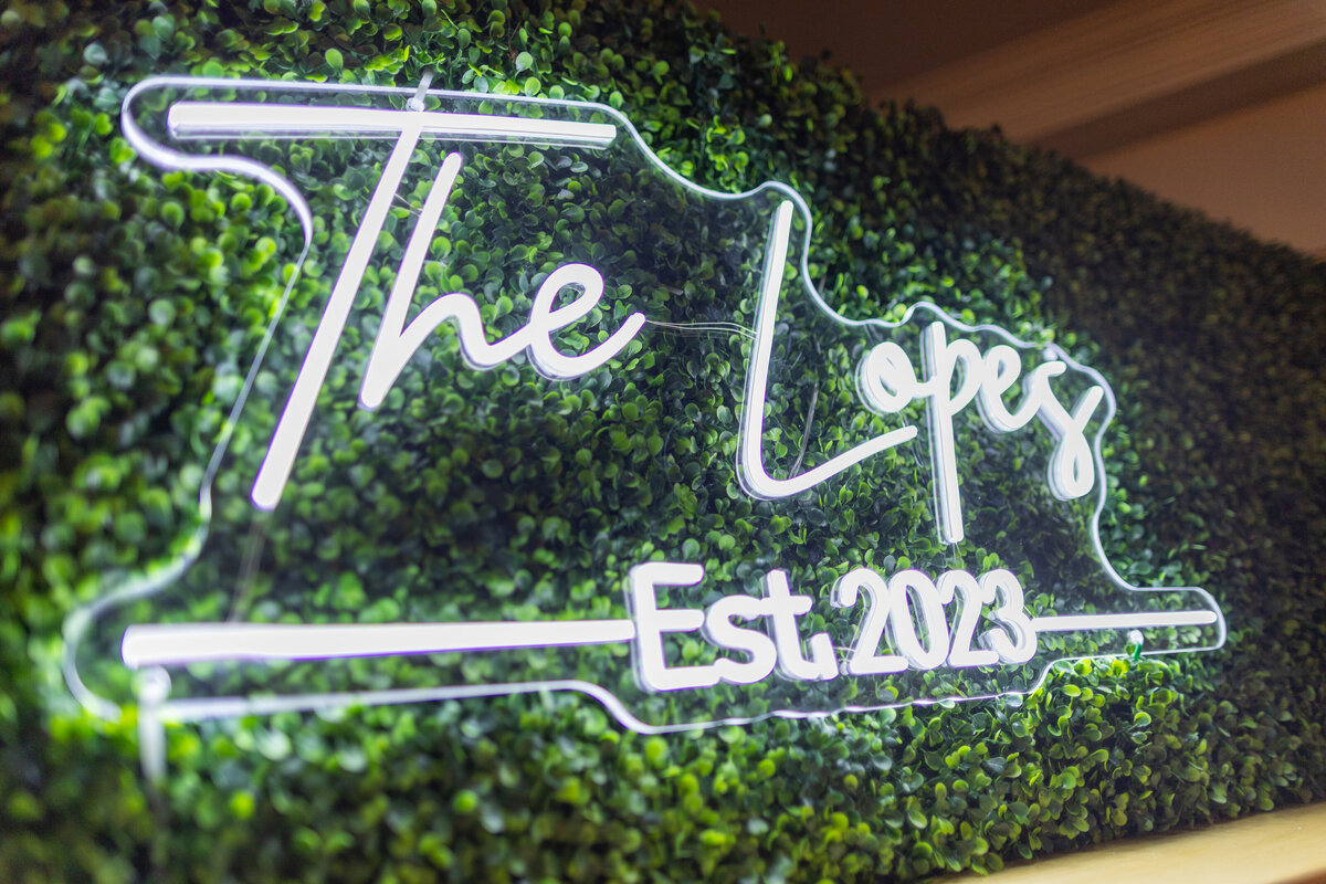 White neon "The Lopes EST. 2023" sign on greenery