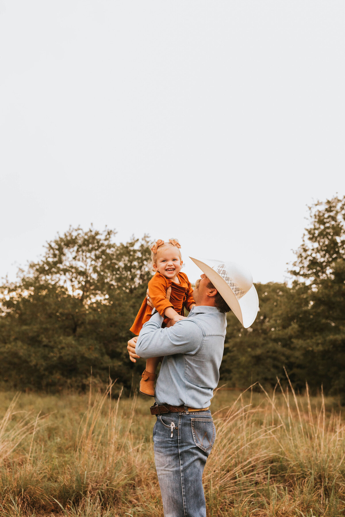 Father in a cowboy hat holding up his happy little girl