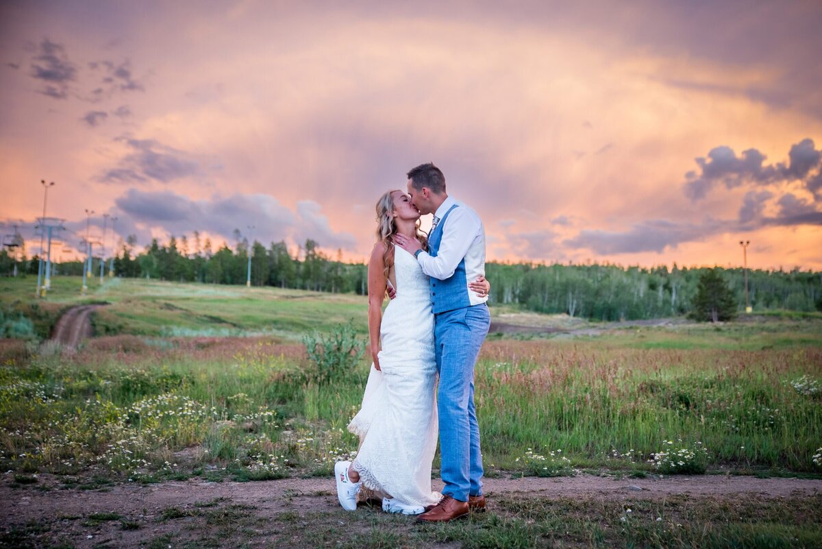 A groom grabs his bride's face as they share a kiss during sunset.