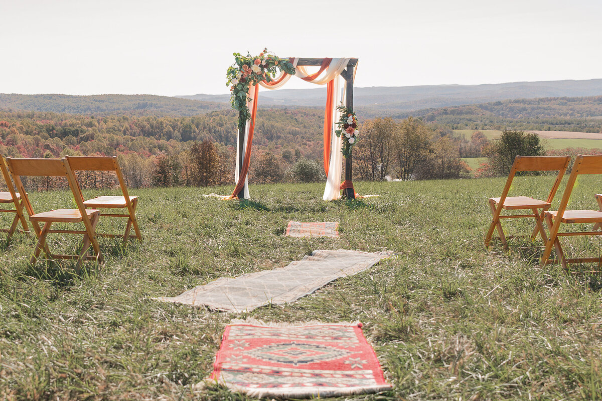 Outdoor fall wedding ceremony with wooden arbor draped in terracotta, white and cream fabric, overlooking rolling hills in southwestern Pennsylvania.