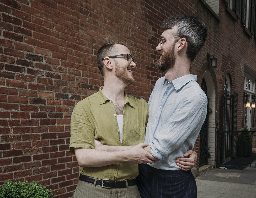 Two grooms smiling and holding each other on a NYC street in Greenwich Village. Photograph by Mira Park Photography.