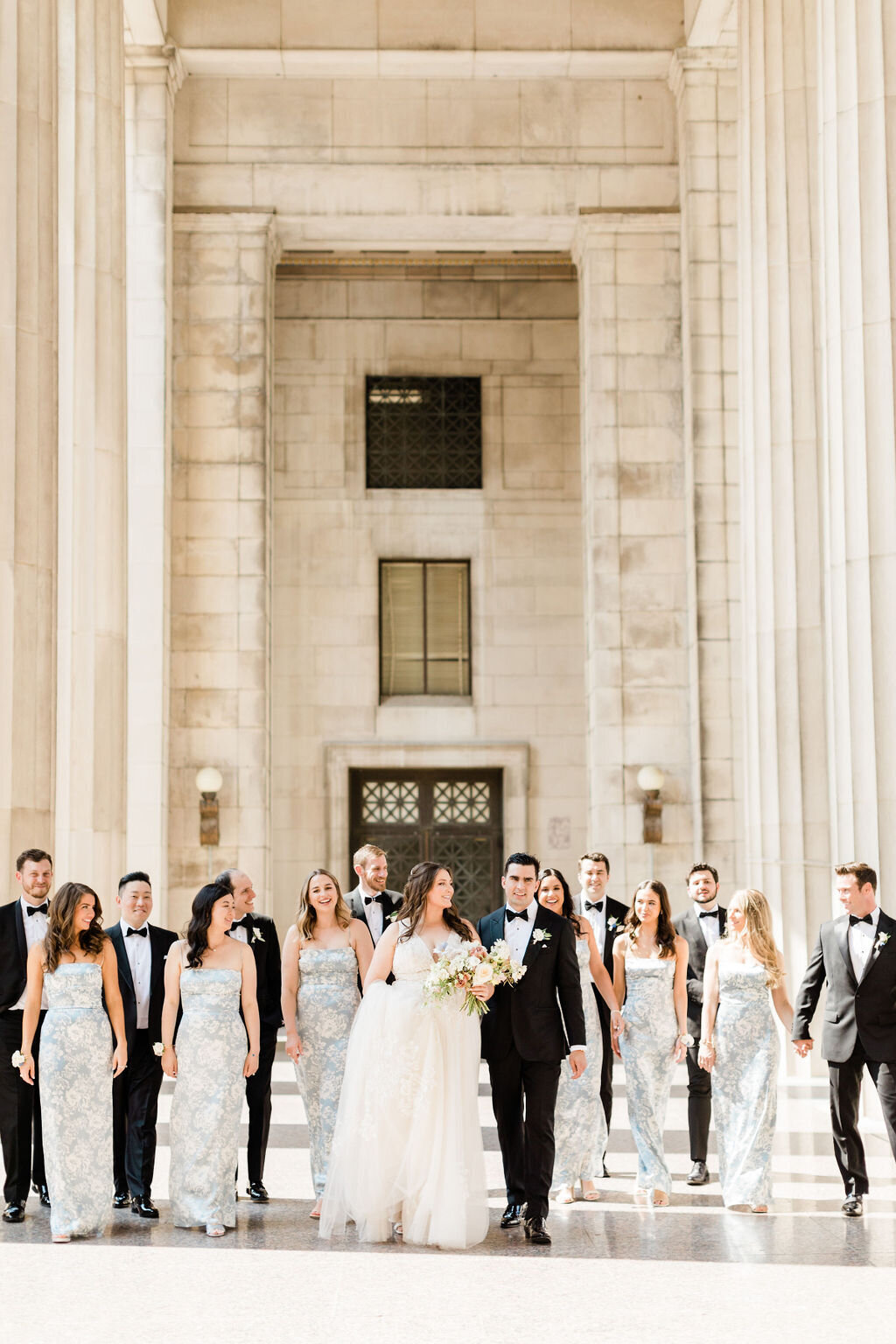 Bride and groom walk with wedding party under stone exterior of Hermitage Hotel Nashville