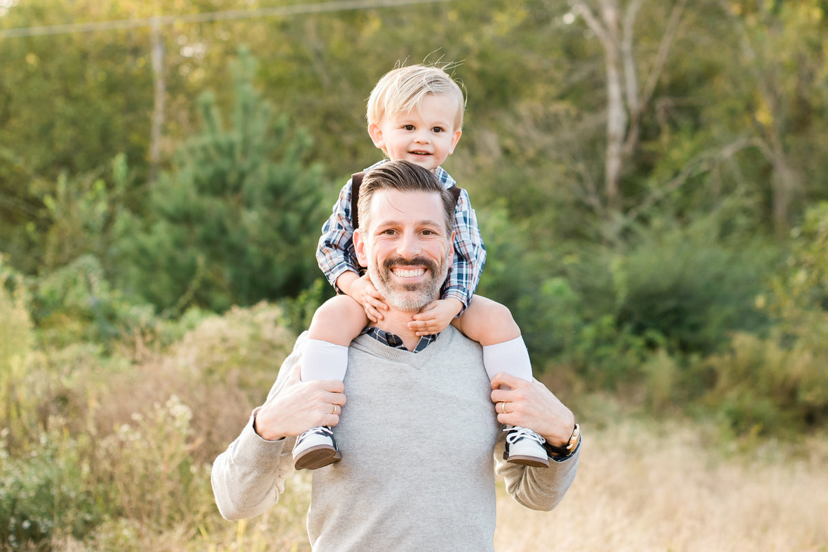 Toddler sits on dad's shoulders and smile during a Raleigh family photography session. Photographed by Raleigh NC Family Photographer A.J. Dunlap Photography.