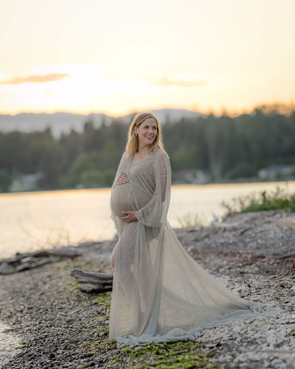 Beth Benecki photographs a mom-to-be glows in a sheer golden dress, set against a stunning PNW sunset.