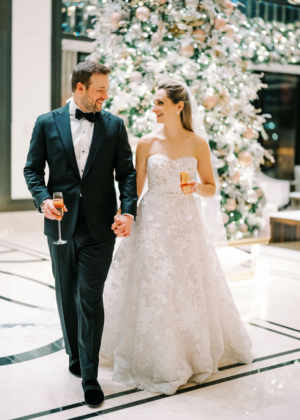 Bride and groom walking with their drinks holding hands. 