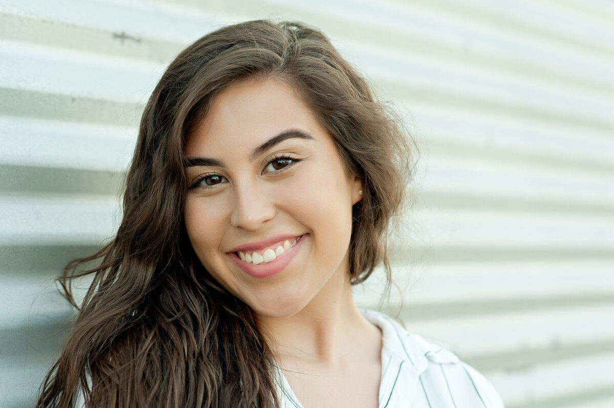 high school senior girl with brown hair and striped shirt leaning up against aluminum wall in orlando
