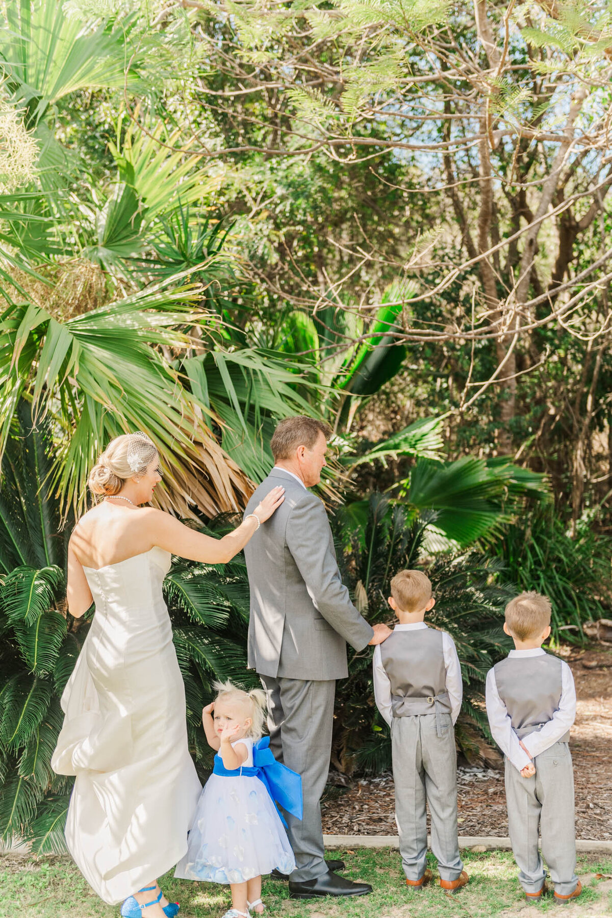Bride, taps and groom on the shoulder during their first look, surrounded by their kids on their wedding day