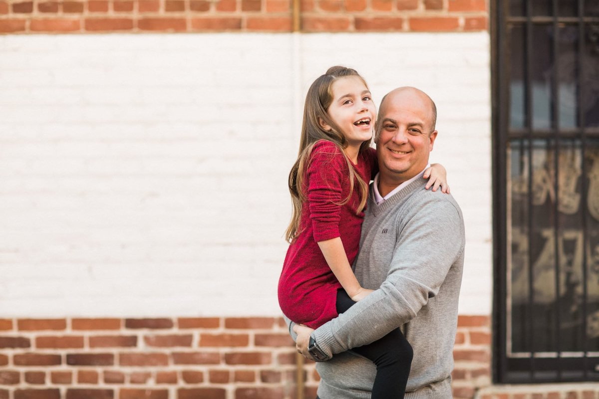 A dad poses with his young daughter in his arms as they both give big smiles