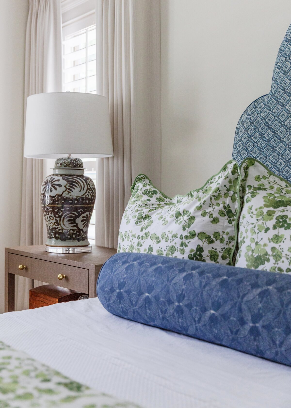 oyster creek studios oak forest remodel  wooden accent table with lamp and blue pillow on bed with green floral bedspread in bedroom