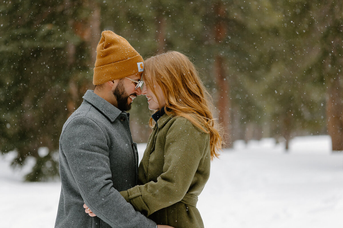 A couple touches their heads together while it snows around them during their Colorado Engagement Session.