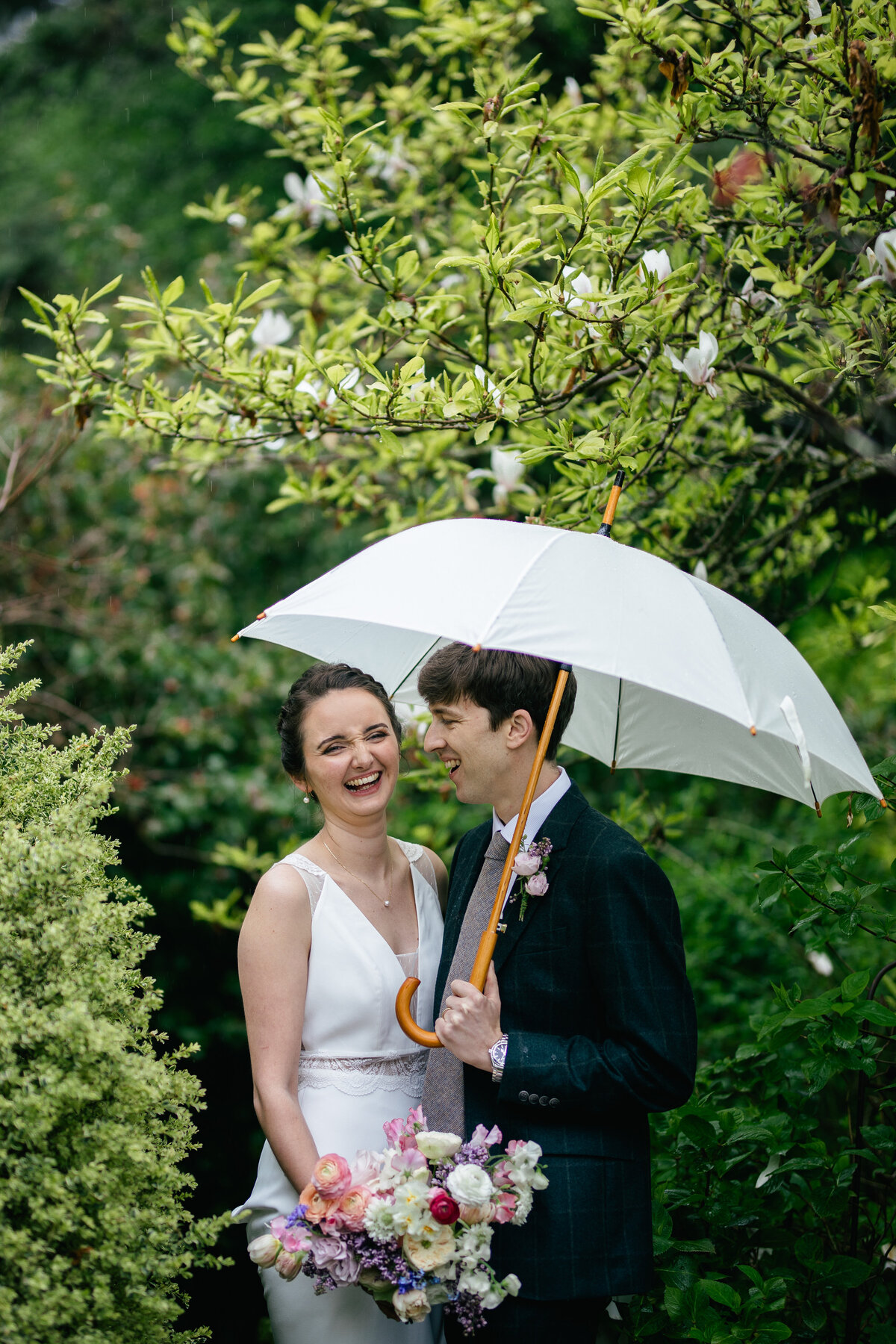 bride and groom pose under umbrella for thier wedding photographer during the rain